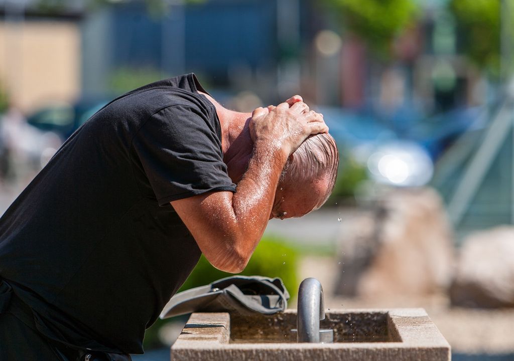 persona refrescándose en un día de calor extremo en una fuente de agua pública