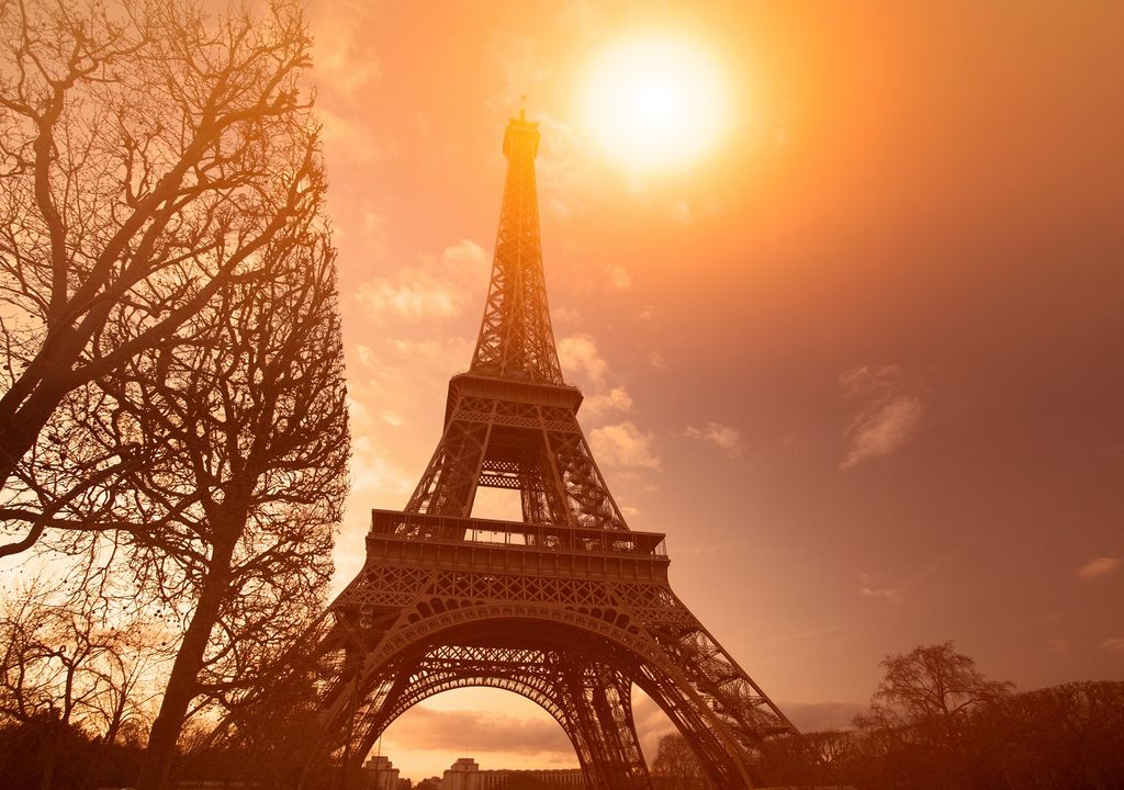 Imagen de la torre Eiffel bajo un cielo en tonos anaranjados, junto a árboles sin hojas