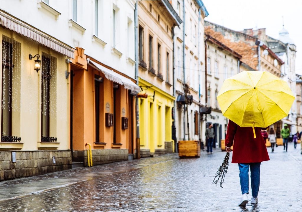 Mujer con abrigo y paraguas caminando en la ciudad bajo la lluvia