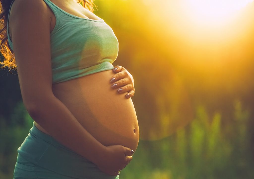 Mujer embarazada en la naturaleza fondo de sol