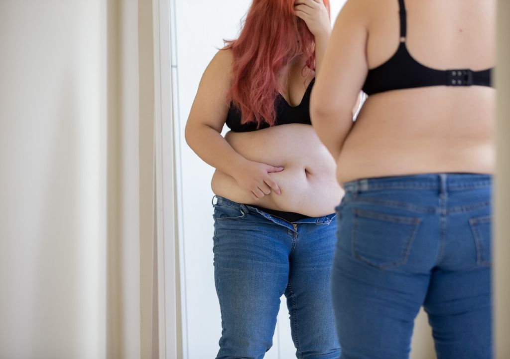 Mujer adolescente frente al espejo cubriendo su rostro, cabello colorado, sostén y jeans. Mujer adolescente frente al espejo cubriendo su rostro, cabello colorado, sostén y jeans.