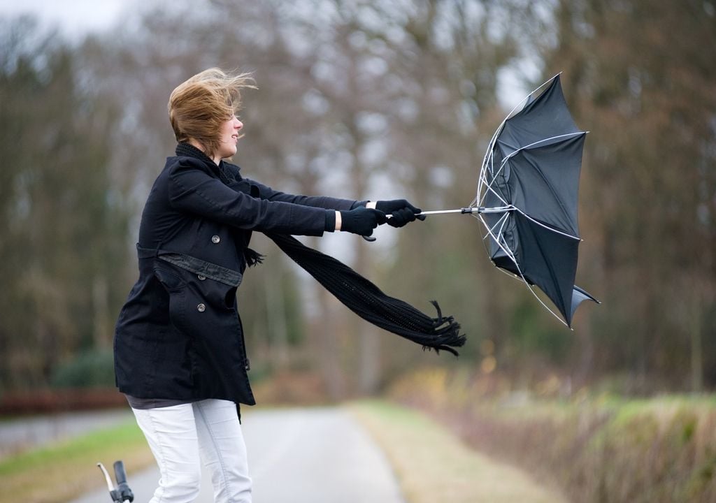 Mujer con paraguas volteado y fuerte viento