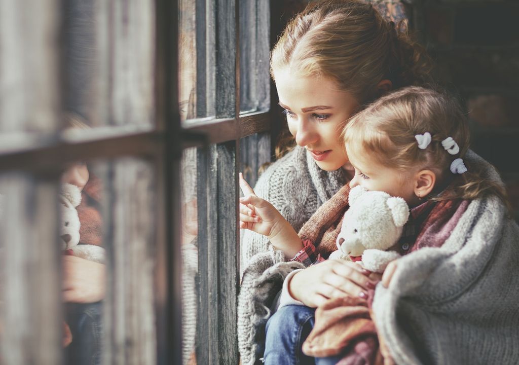 Madre e hija mirando hacia afuera por una ventana Madre e hija mirando hacia afuera por una ventana