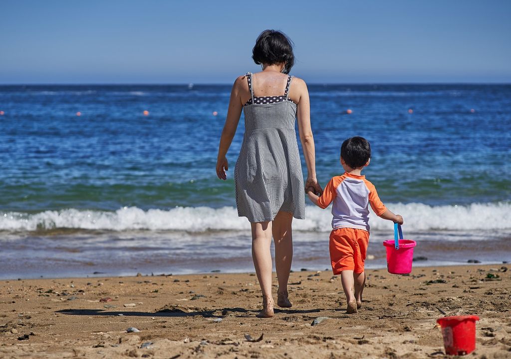 mujer y niño caminando hacia el mar