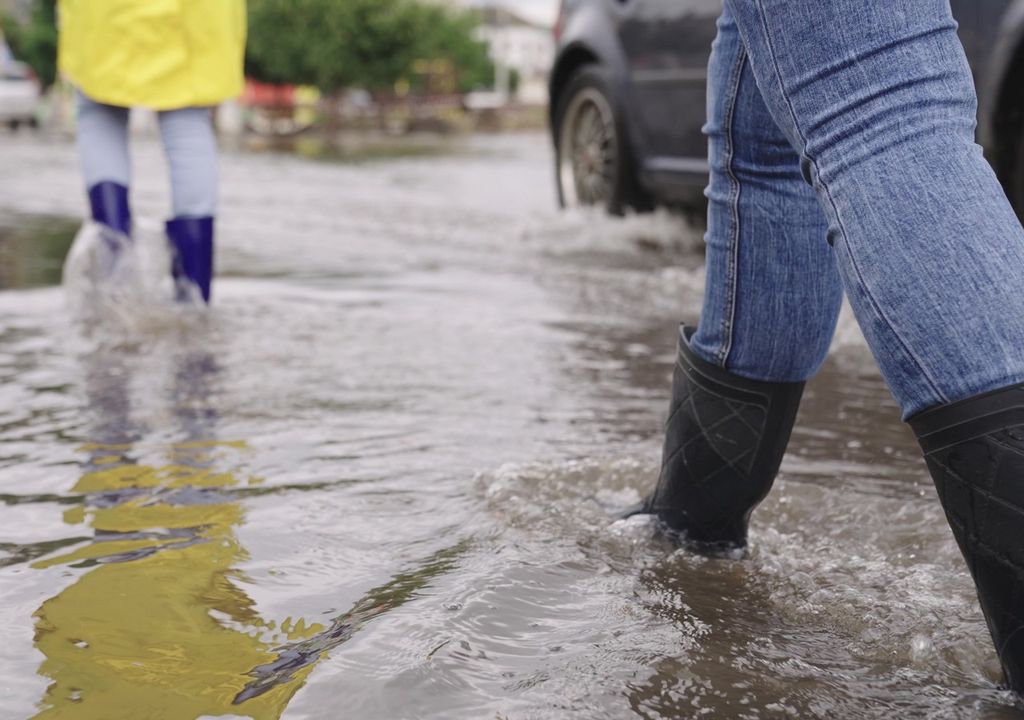 Personas caminando con botas en una calle llena de agua lluvia