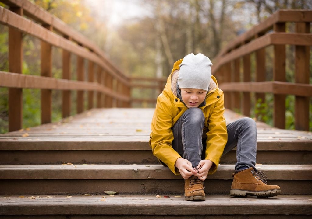 Niño sentado abrochándose el zapato en día frío Niño sentado abrochándose el zapato en día frío