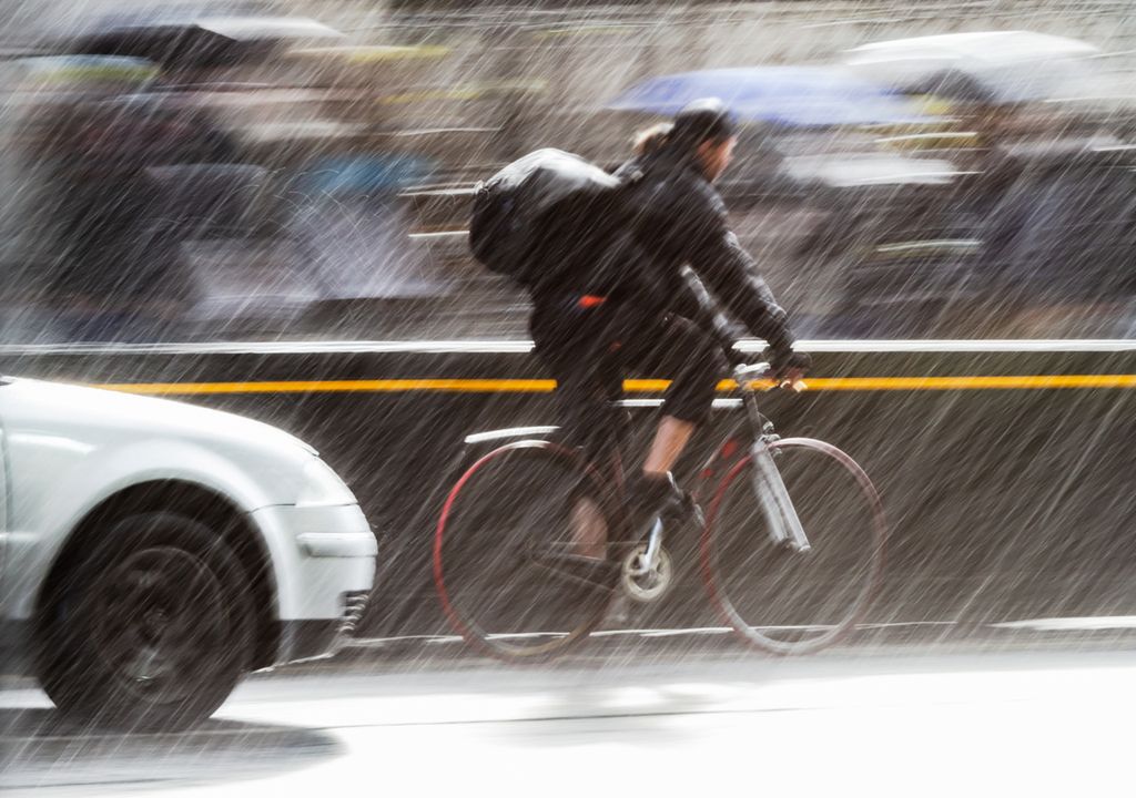 Ciclista enfrentando a chuva nas ruas de uma cidade.