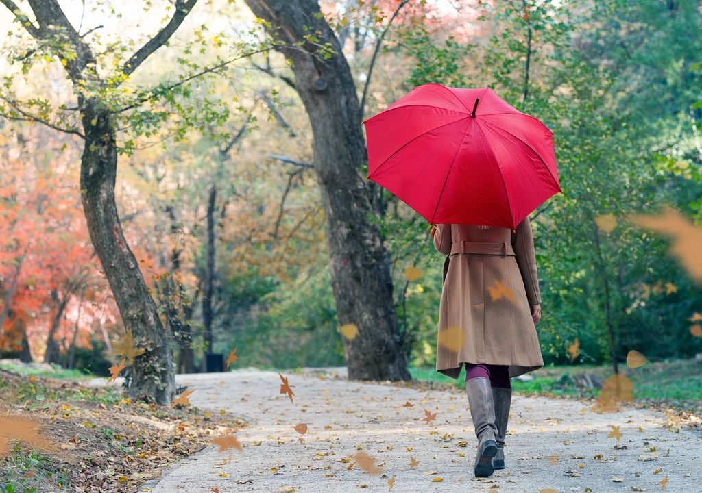 Mujer caminando por un sendero otoñal con paraguas rojo