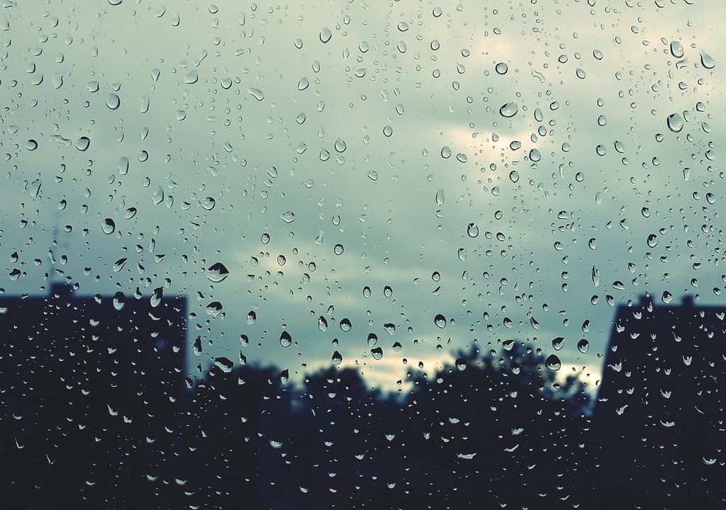 Silueta de árboles y casas a través de una ventana mojada por la lluvia