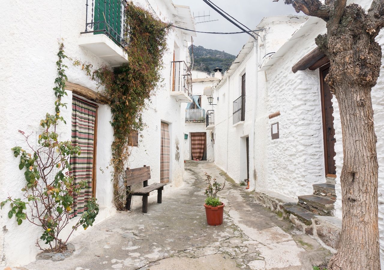 Calle empedrada de Capileira, donde los antiguos tinaos aún sirven de refugio frente a las nevadas invernales y las chimeneas troncocónicas, únicas en La Alpujarra, coronan las casas como herencia directa de las construcciones bereberes.
