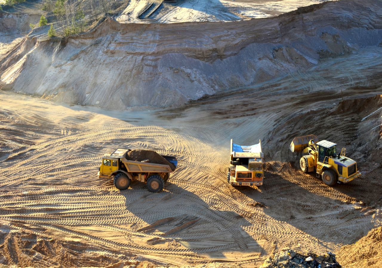 Imagem de uma pedreira que no seu processo de produção utiliza três exemplos de máquinas movidas a combustíveis fósseis, cujas emissões têm impactes nos padrões climáticos.