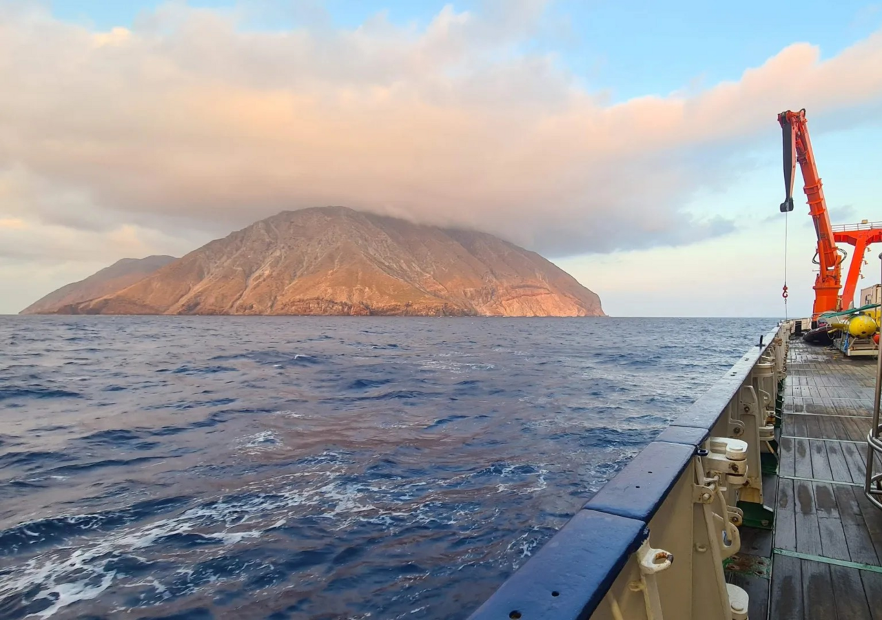 Während der METEOR-Fahrt vor der griechischen Insel Milos: die Wasserschöpfer-Rosette und das AUV MARUM-SEAL an Deck, im Hintergrund die unbewohnte Vulkaninsel Antimilos. Bild: MARUM – Zentrum für Marine Umweltwissenschaften, Universität Bremen/S. I. Bühring