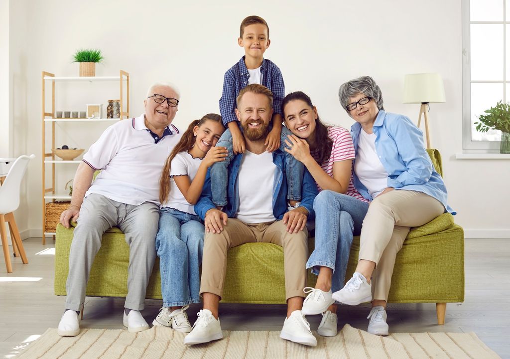 familia, abuelo, abuela, padre, madre, hijo, hija sentados en sofá verde fondo casa