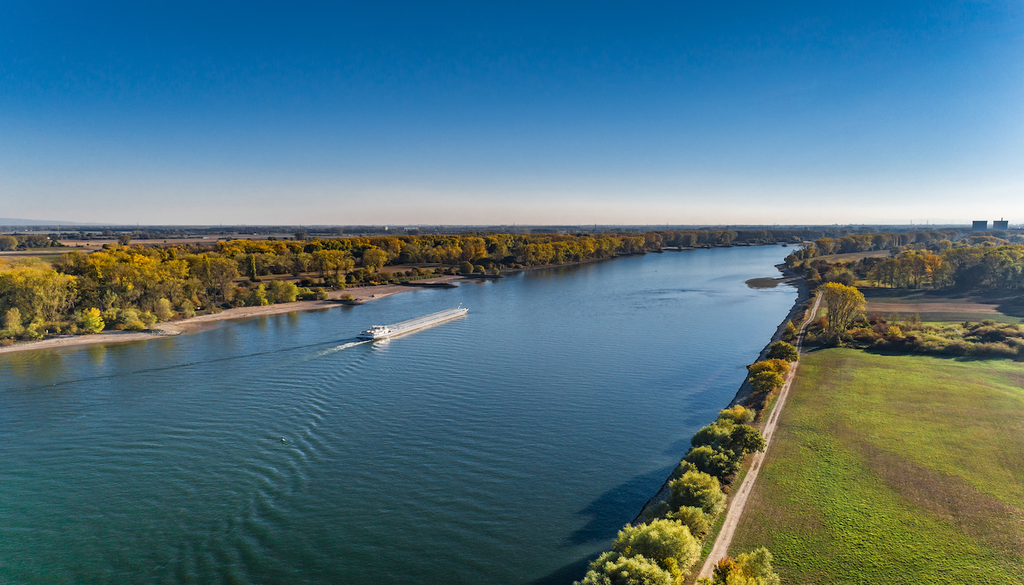 Tanker, Rhein, eingefasste Flussbett, Schifffahrt, Auen? Ein Tanker auf dem Rhein: Das eingefasste Flussbett bietet Raum für die Schifffahrt – doch wo bleibt der Platz für natürliche Auen? Ihre Verbindung zum Fluss ist entscheidend für Wasserrückhalt und Hochwasserschutz.