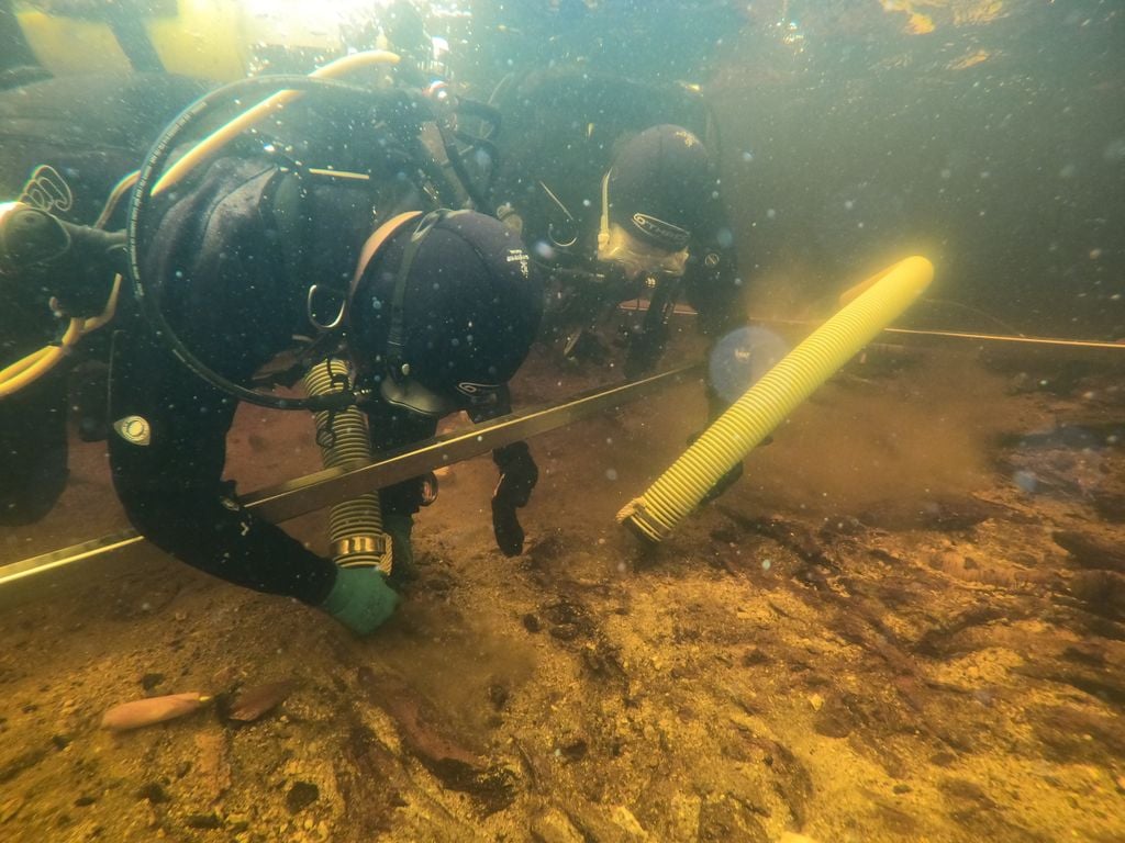 Un buzo excavando el lecho de un lago, bajo el agua, con una bombona de oxígeno amarilla. Excavaciones submarinas en el lago.