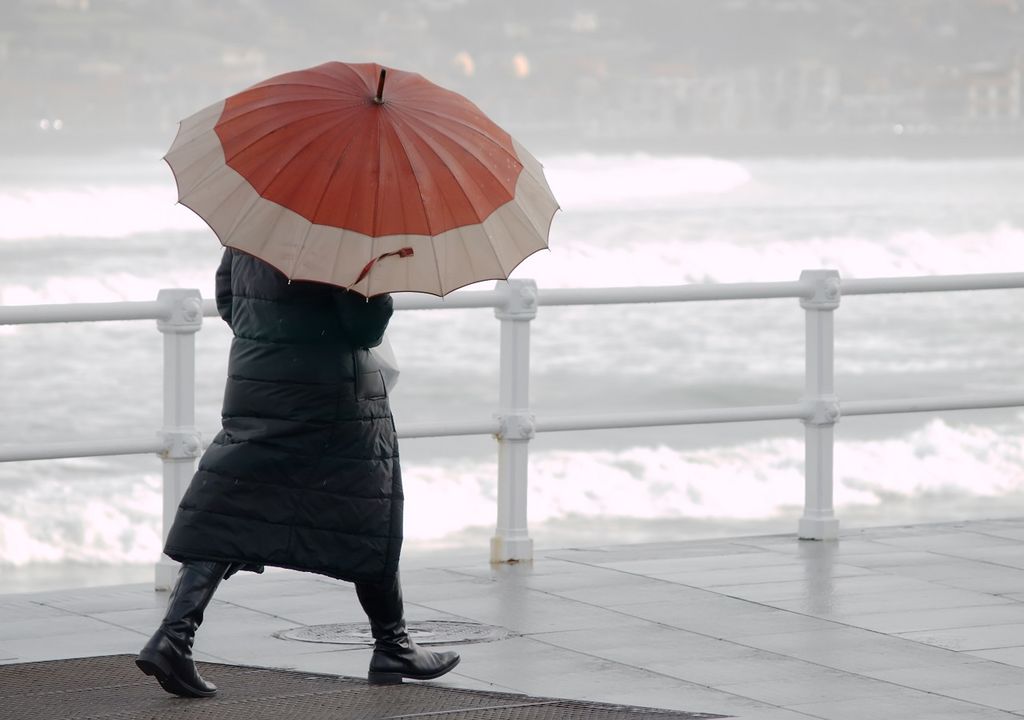 Persona caminando con paraguas; mar agitado; lluvias
