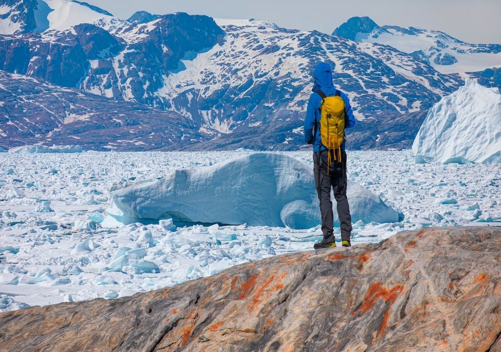 A hiker worriedly observes a melting glacier, consulting historical maps that show its sudden reduction. Tiniteqilaaq, Sermilik Fjord, East Greenland.