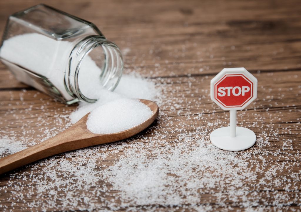 Frasco de vidrio volcado con azúcar y pequeño letrero con "stop"