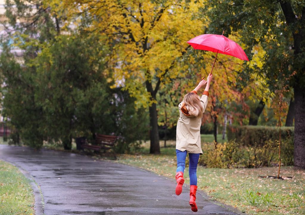 Mujer con paraguas rojo saltando bajo la lluvia