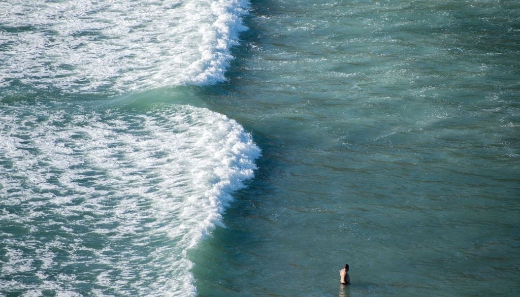 Un turista che fa il bagno vicino a una pericolosa corrente di risacca presso la spiaggia di Piha ad Auckland, in Nuova Zelanda