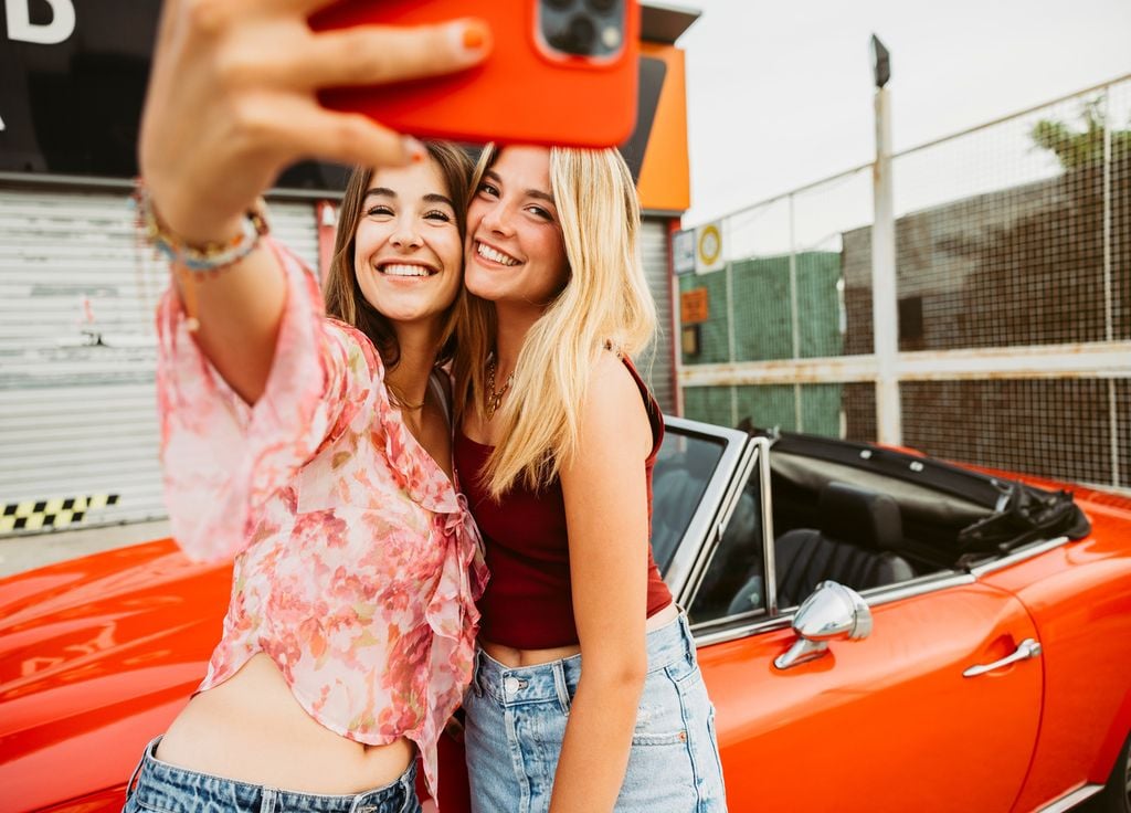 Dos mujeres jóvenes comparten una selfie frente a un auto descapotable. Dos mujeres jóvenes comparten una selfie frente a un auto descapotable.