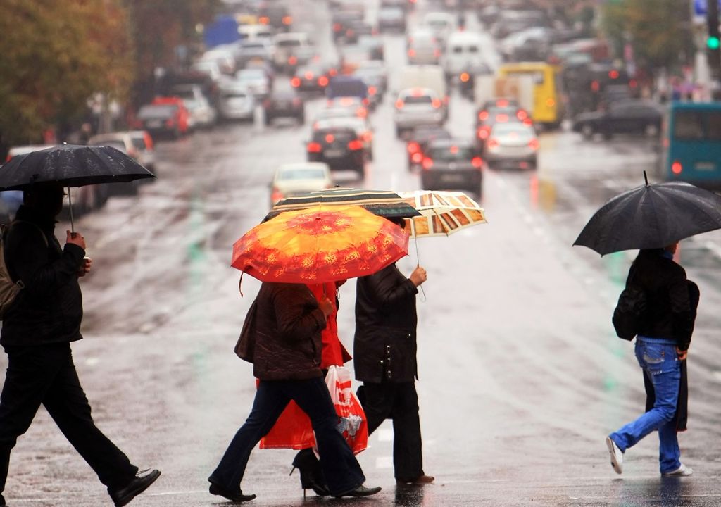 personas con paraguas cruzando una calle en día de lluvia