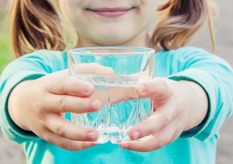Niña sosteniendo un vaso con agua transparente entre sus manos Niña sosteniendo un vaso con agua transparente entre sus manos