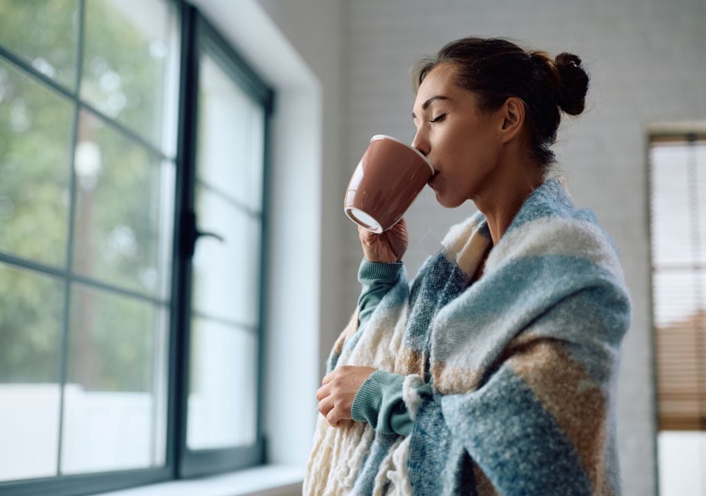 Mulher agasalhada bebendo chá quente em casa.