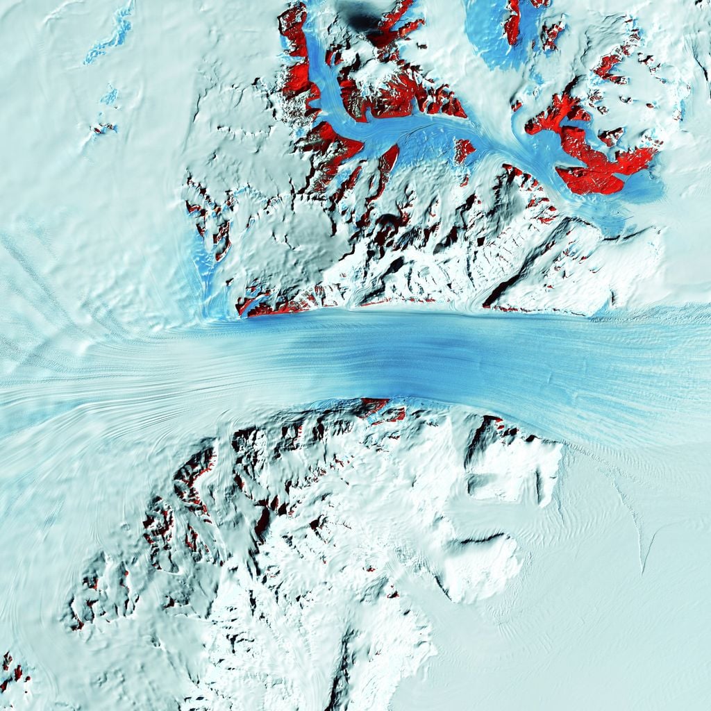 El glaciar Byrd, de rápido movimiento, atraviesa la cordillera Transantártica, fluyendo desde la meseta polar (izquierda) hasta la plataforma de hielo de Ross (derecha). En esta imagen satelital infrarroja a color, las manchas rojas marcan la roca expuesta. Los investigadores proponen que el levantamiento de las montañas propició la formación de la capa de hielo. Fotografía del Servicio Geológico de los Estados Unidos.
