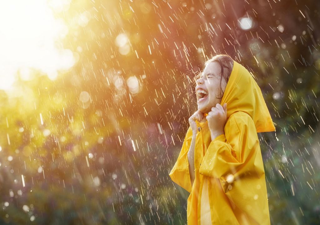 Niña con impermeable amarillo bajo la lluvia fondo sol