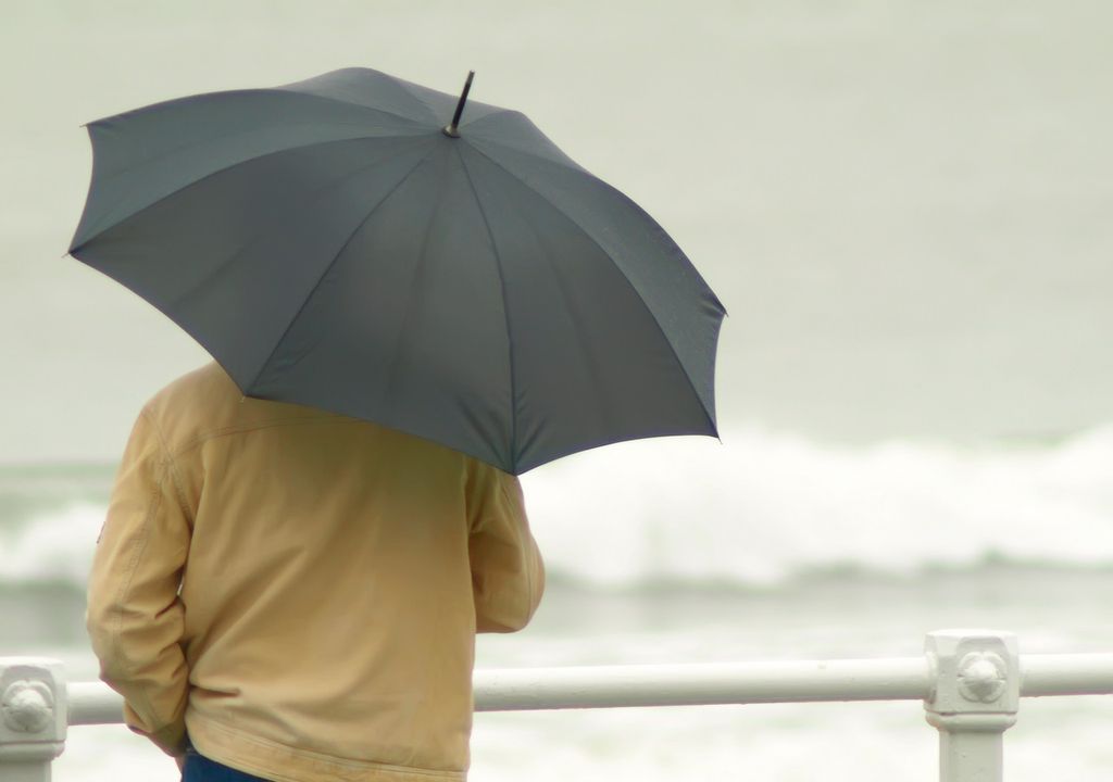 persona con paraguas mirando el mar