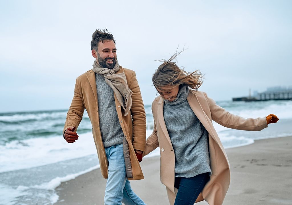 Pareja joven abrigada y contenta caminando por la playa fondo mar