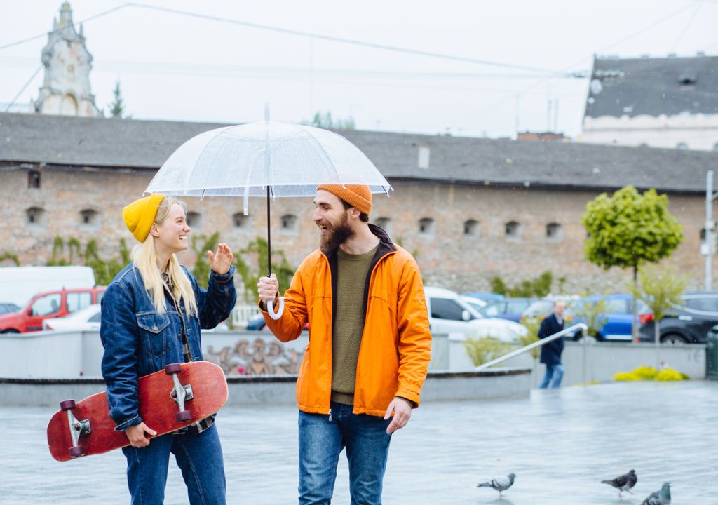 Ein junger Mann und eine junge Frau laufen mit einem Regenschirm durch Berlin. Ein Skateboard in der Hand passt das herbstliche Wetter bestens für Outdoor-Aktivitäten. Ein junger Mann und eine junge Frau laufen mit einem Regenschirm durch Berlin. Ein Skateboard in der Hand passt das herbstliche Wetter bestens für Outdoor-Aktivitäten.