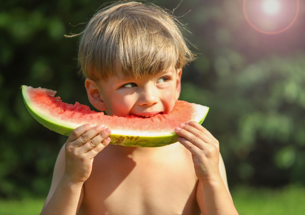 Ein Junge beist in ein Stück Wassermelone. Es ist Sommer und es ist heiß, Badesachen an und dann Sprung ins kühle Nass.