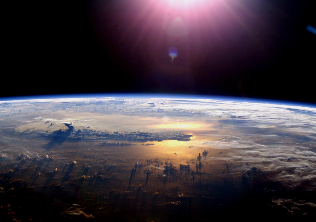 superficie del planeta vista desde el espacio, con el sol iluminando desde un punto alto
