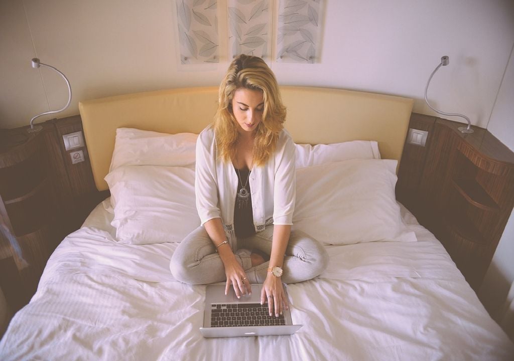 Mulher sentada na cama e a trabalhar no computador Mulher sentada na cama e a trabalhar no computador