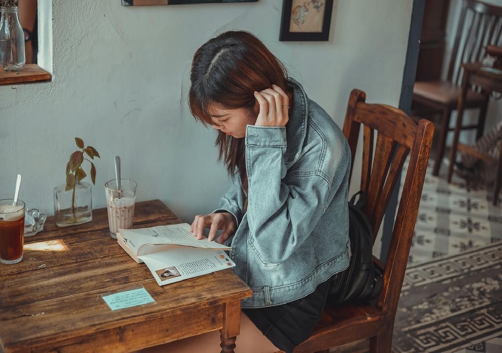 Jovem mulher lê um livro sentada numa mesa de café Jovem mulher lê um livro sentada numa mesa de café