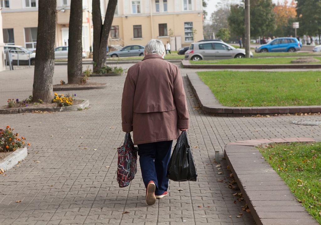 adulto mayor caminando con la espalda curvada, mientras lleva bolsas en sus manos