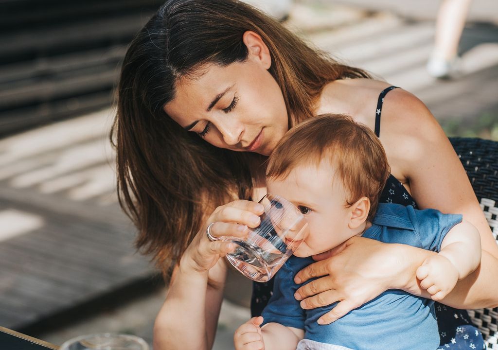 Madre le da agua a su hijo con un vaso de vidrio