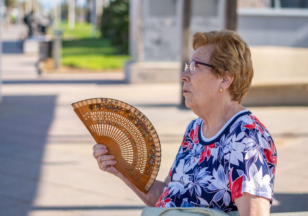 Mujer mayor con abanico por calor fondo con área verde