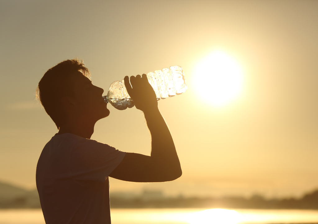 persona bebiendo agua, con el sol de fondo persona bebiendo agua, con el sol de fondo