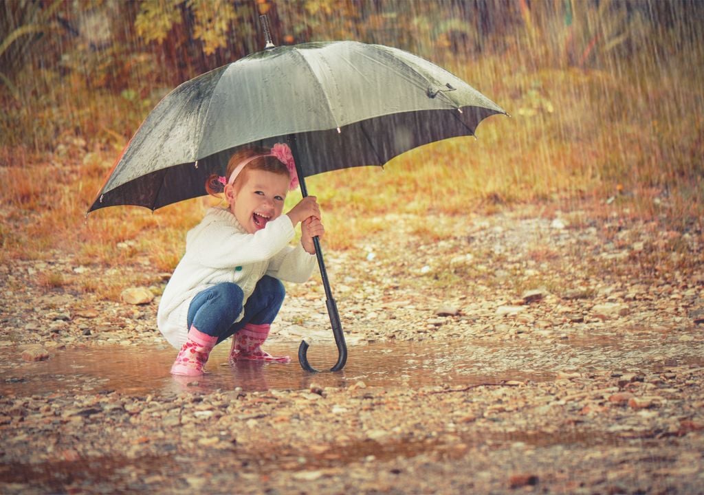 Stepping in puddle with umbrella during rainfall.