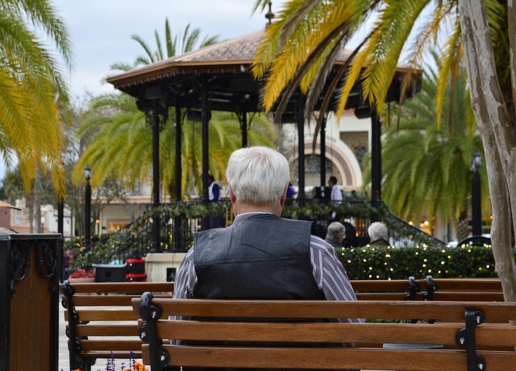 persona de cabello blanco sentada en el banco de una plaza