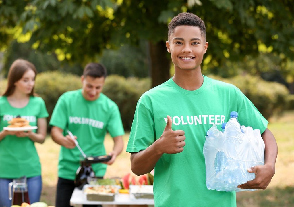 Joven voluntario con botellas de aguas en su brazo izquierdo fondo paisaje con otros voluntarios