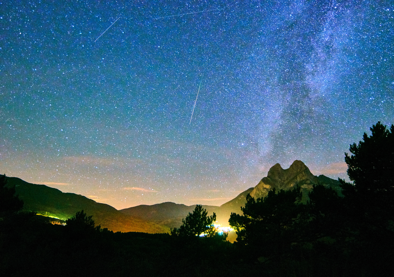 Cielo nocturno bajo las Perseidas: así se aprecia la lluvia de meteoros sobre un paisaje montañoso, con destellos fugaces cruzando la Vía Láctea. Un espectáculo natural que cada agosto nos recuerda lo pequeño —y maravilloso— que es nuestro lugar en el cosmos.