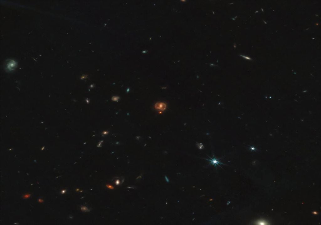 Os pequenos pontos vermelhos são buracos negros jovens envoltos num casulo de gás que estão a consumir para crescerem. Crédito Imagem: Darach Watson/James Webb Space Telescope