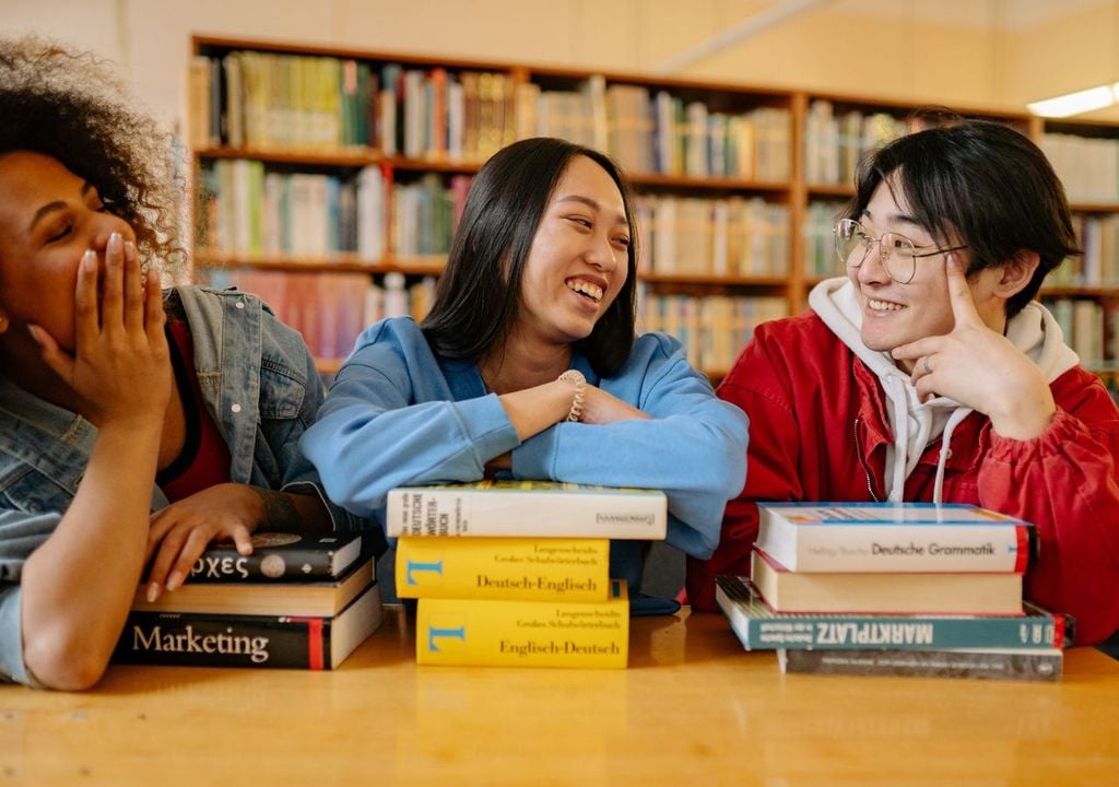 Tres jóvenes de distintos países conversando en una biblioteca