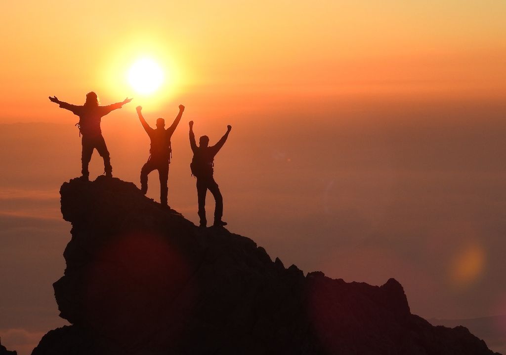 Três pessoas no topo de uma colina comemorando o nascer do sol