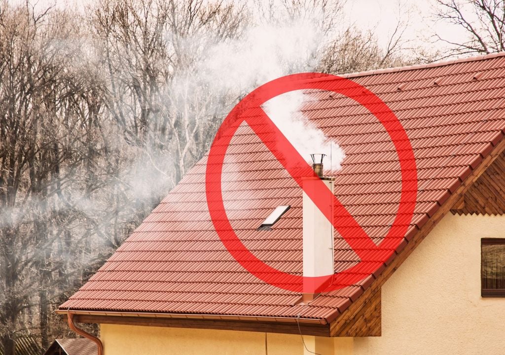 Chimenea en casa emitiendo humo visible y un símbolo de prohibición