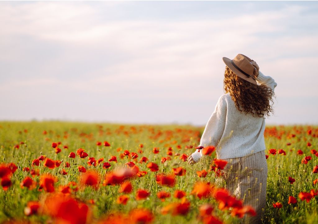 Mujer caminando en un campo de flores rojas fondo cielo con nubes